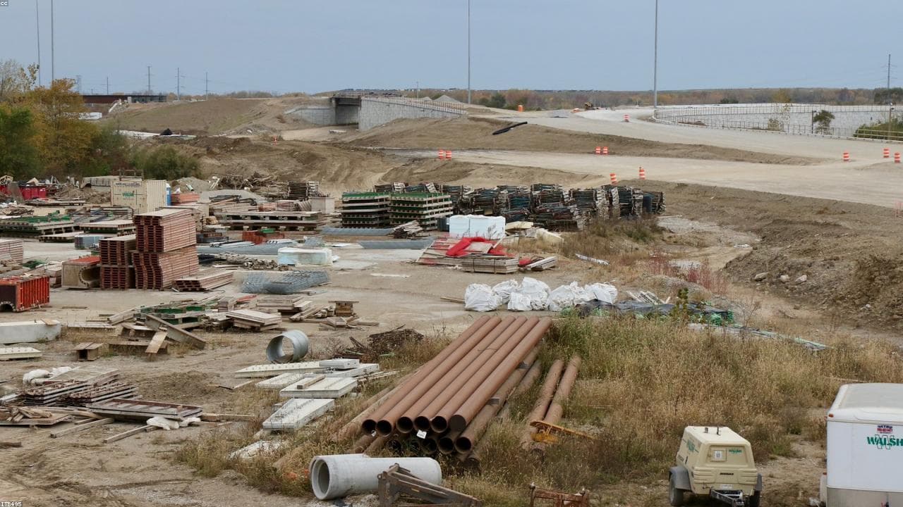 A highway construction laydown yard with staged pipe, precast, and materials