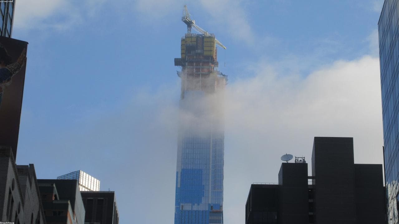 A skyscraper under construction with a tower crane emerging from low cloud