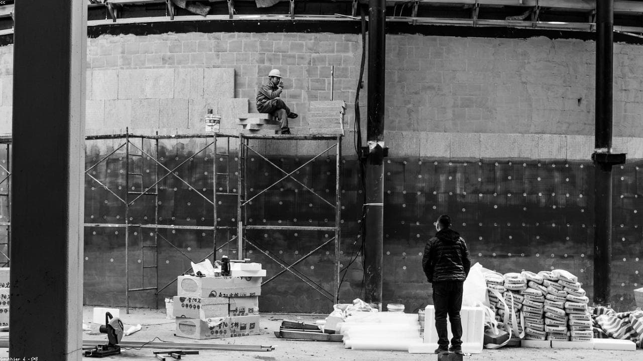 A construction worker resting on scaffolding at an active jobsite, in black and white